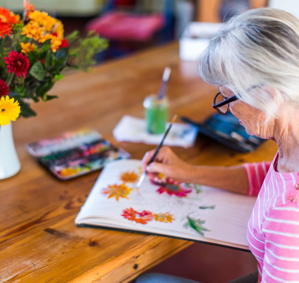 Senior woman painting colorful flowers during a creative activity at Village on the Park Denton.